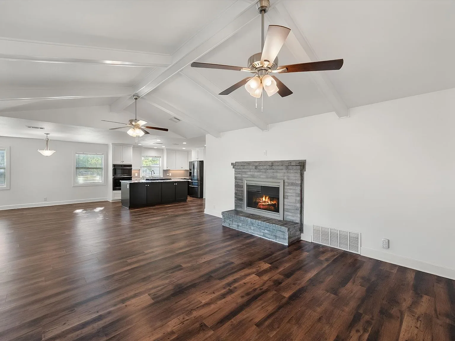 Wide living room view with stone fireplace and open kitchen with dark island