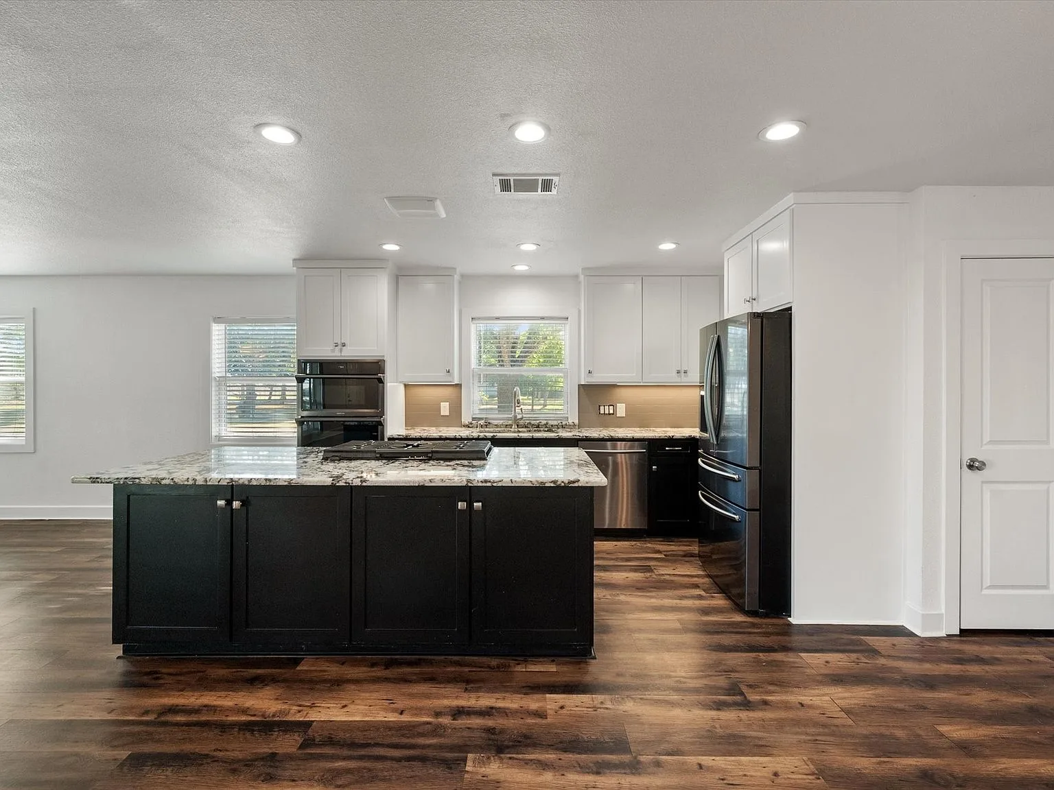 Kitchen with black island, granite countertop cooktop and stainless appliances