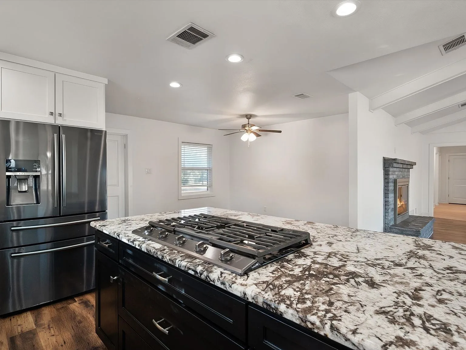 Wide kitchen view with granite island, gas cooktop and white upper cabinetry