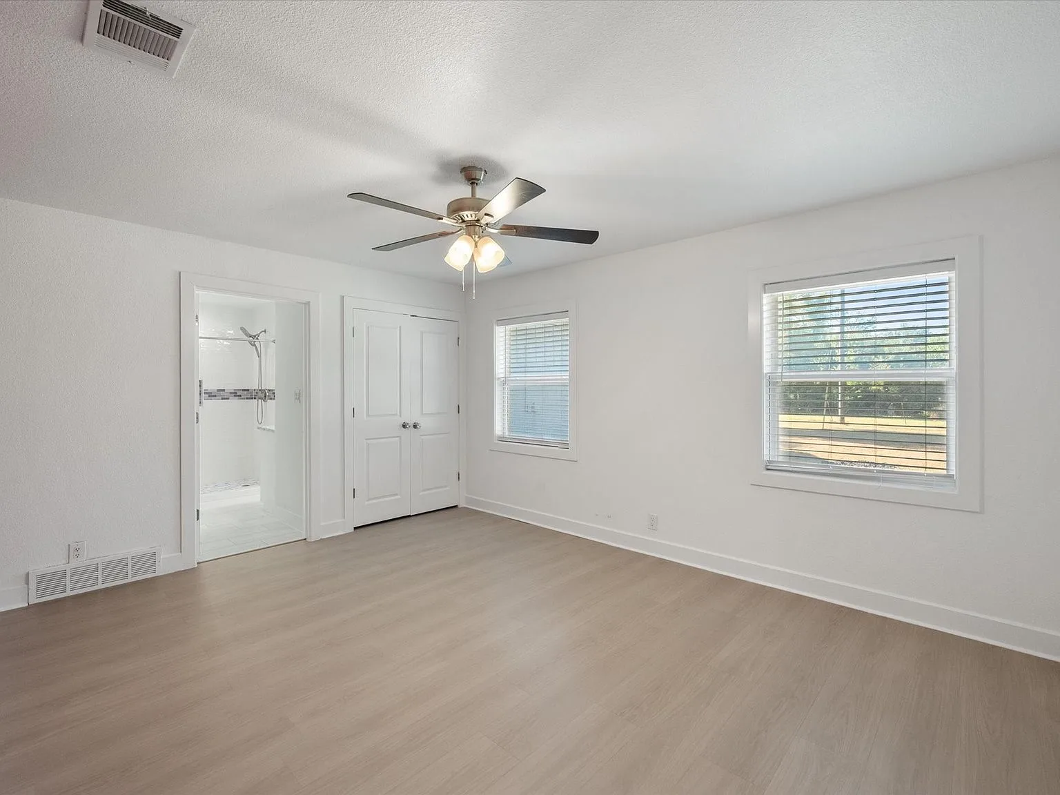 Wide view of the renovated primary bedroom with bright windows and light flooring