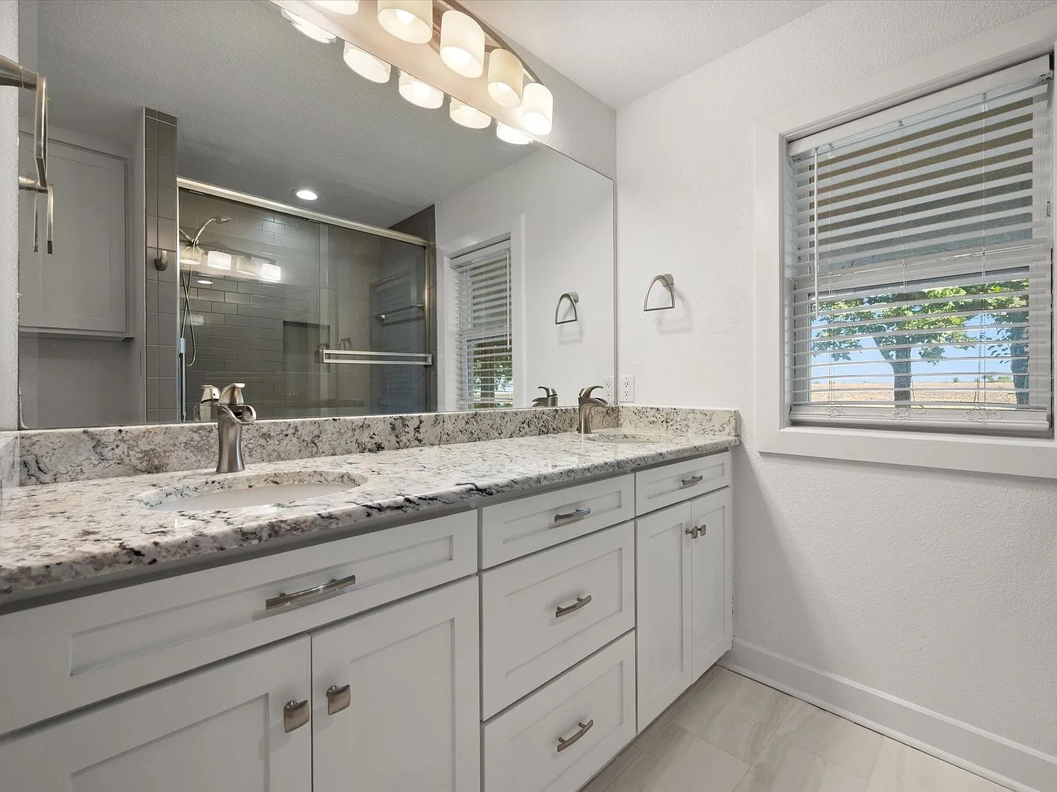 Renovated bathroom vanity with glass-enclosed shower reflected in the mirror
