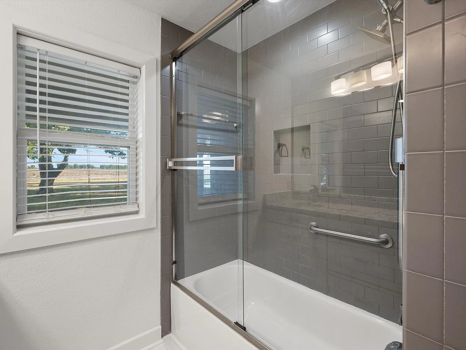 Renovated tub and shower with glass door and subway-style tile