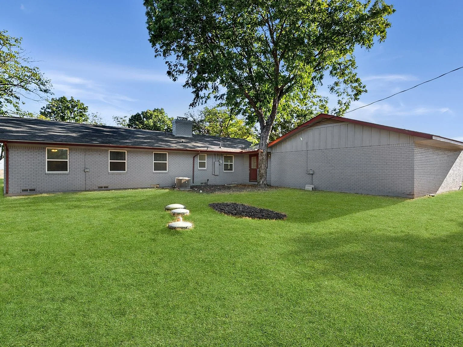 Backyard of the ranch home with a spacious lawn and a large mature shade tree