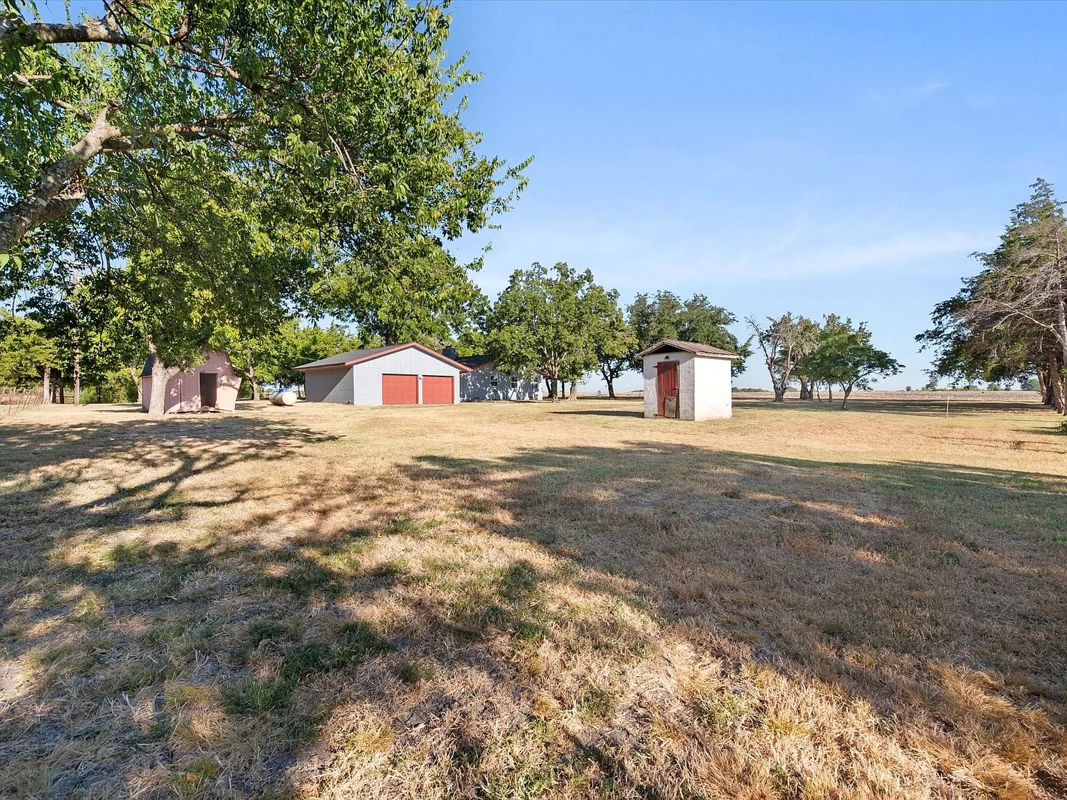 Backyard view across open land toward the detached garage with red doors and outbuildings