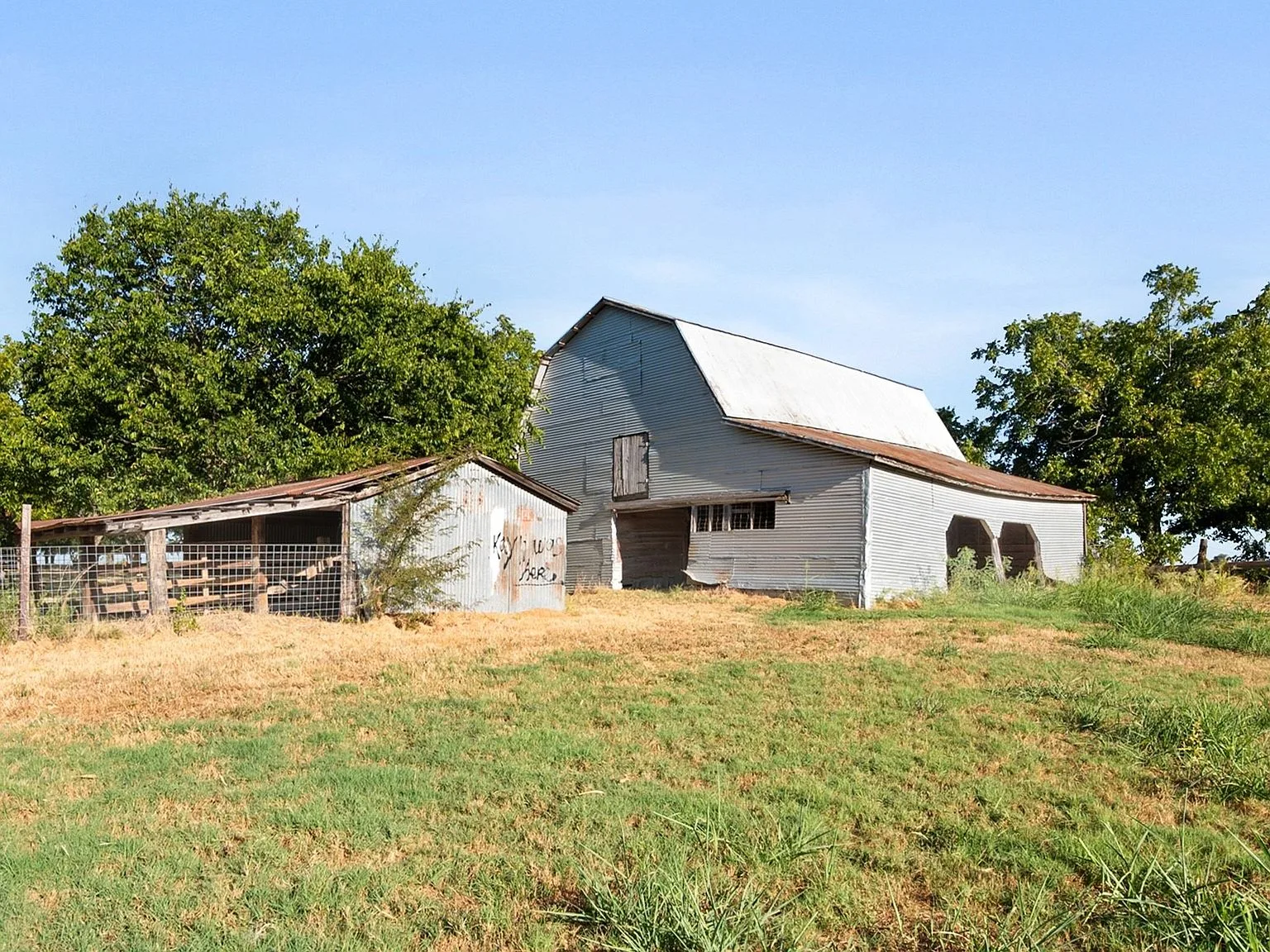 Rustic wooden barn with a metal roof and fenced pasture on the property