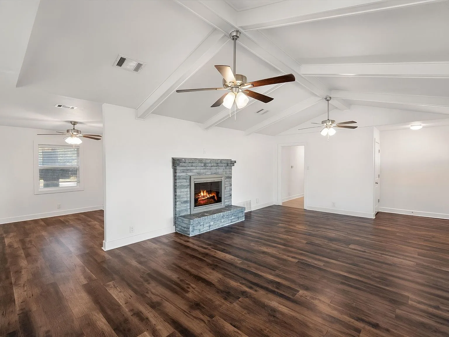 Main living area with wood-look flooring, vaulted beams and brick-faced fireplace