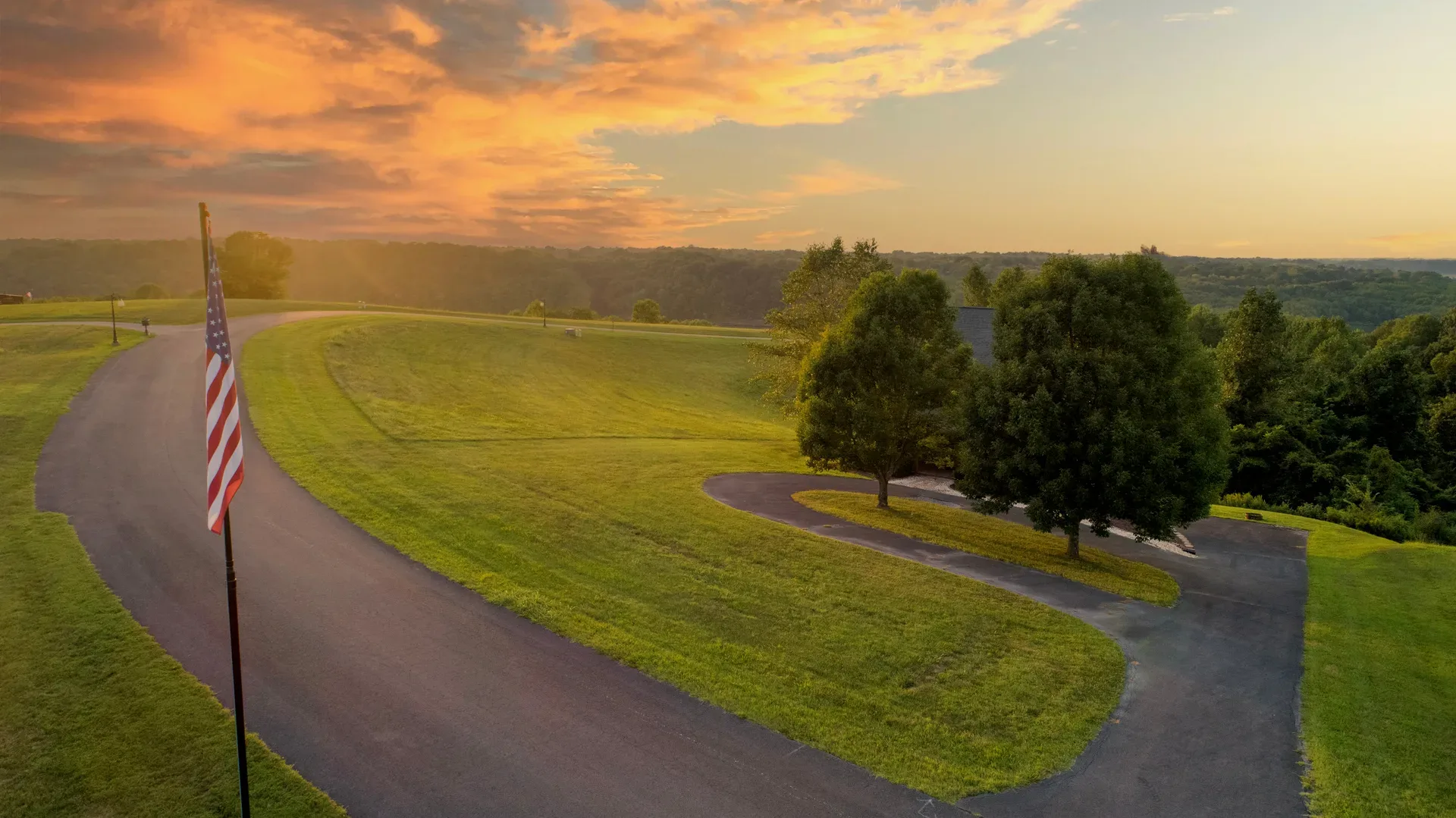 An aerial view of a rural property with rolling lawns and a winding driveway in Kentucky at sunset