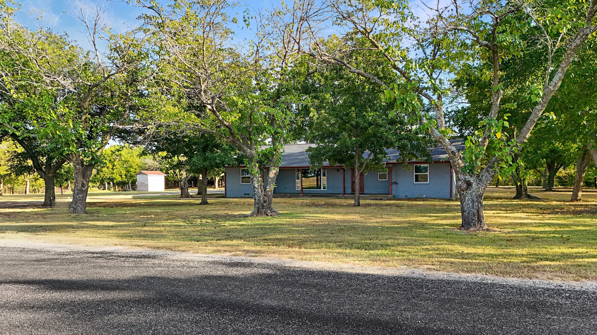 Ranch home exterior facade with mature trees across the grassy front yard