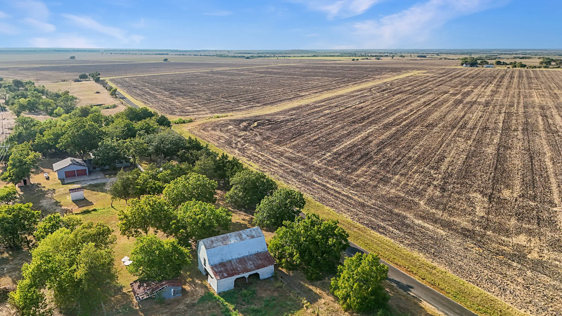 Wide aerial of the acreage with cultivated fields, barn and the house with attached garage