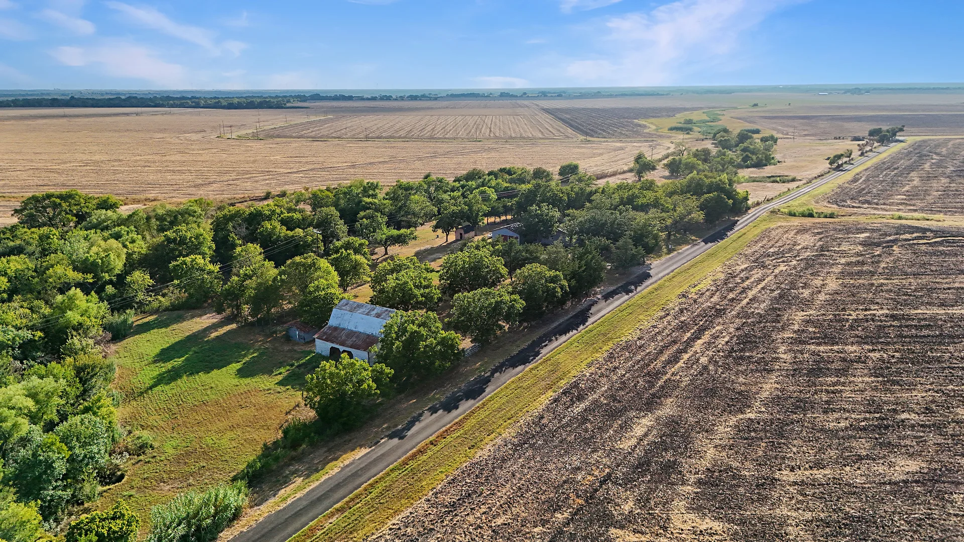 Aerial drone view of the 18+ acres at 917 Goodwyn Rd, with the barn, pasture and paved road running along the property edge