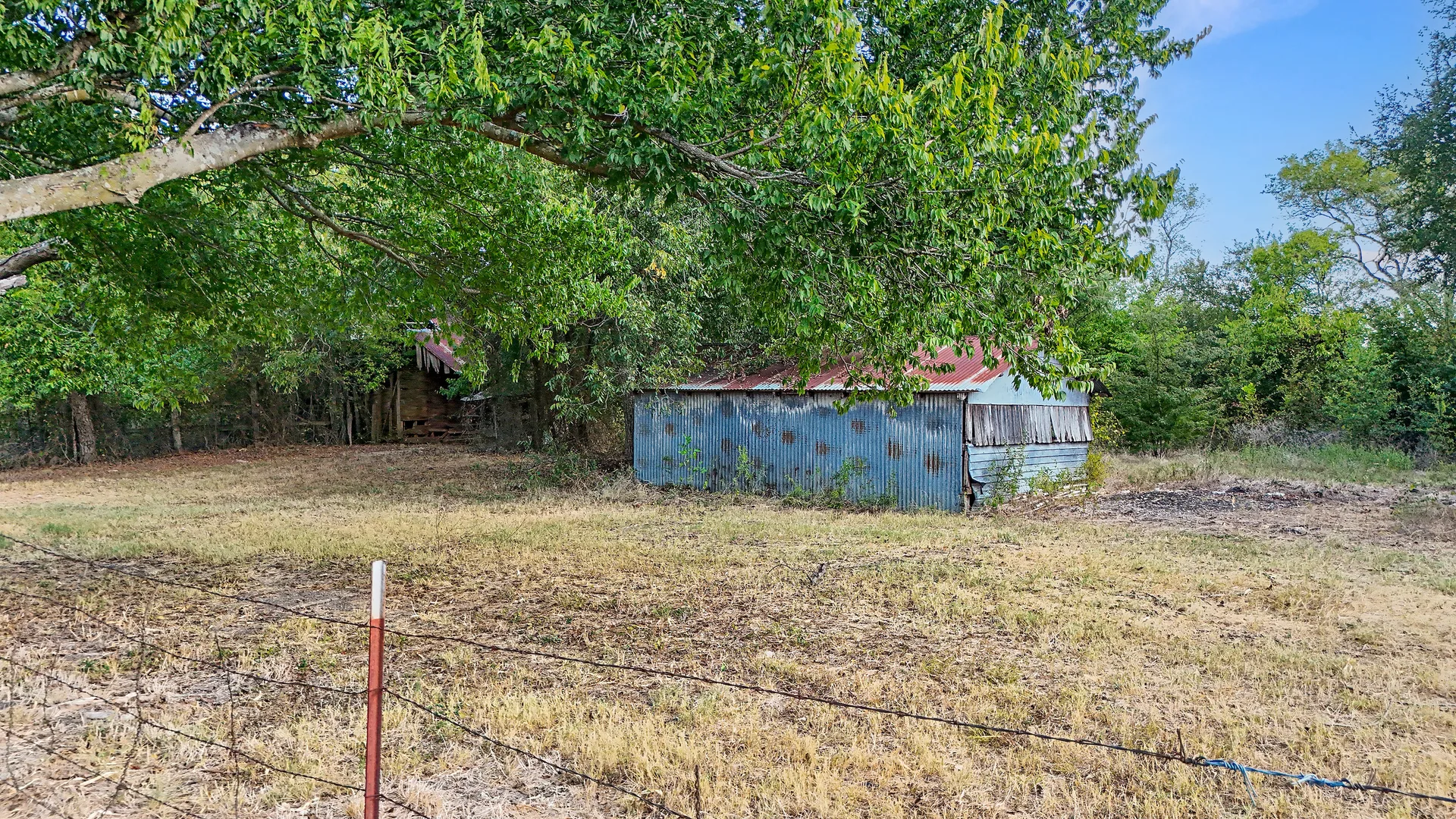Aged blue metal barn with rusted roof behind barbed-wire fencing and pasture