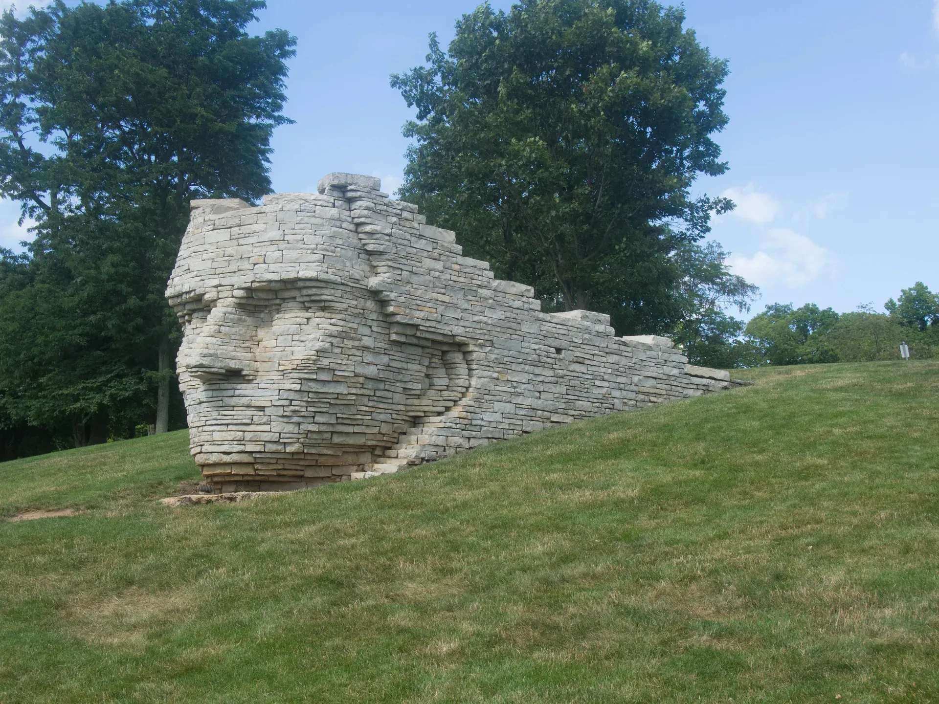 A large outdoor stone sculpture set into a grassy hillside, public art in Dublin Ohio