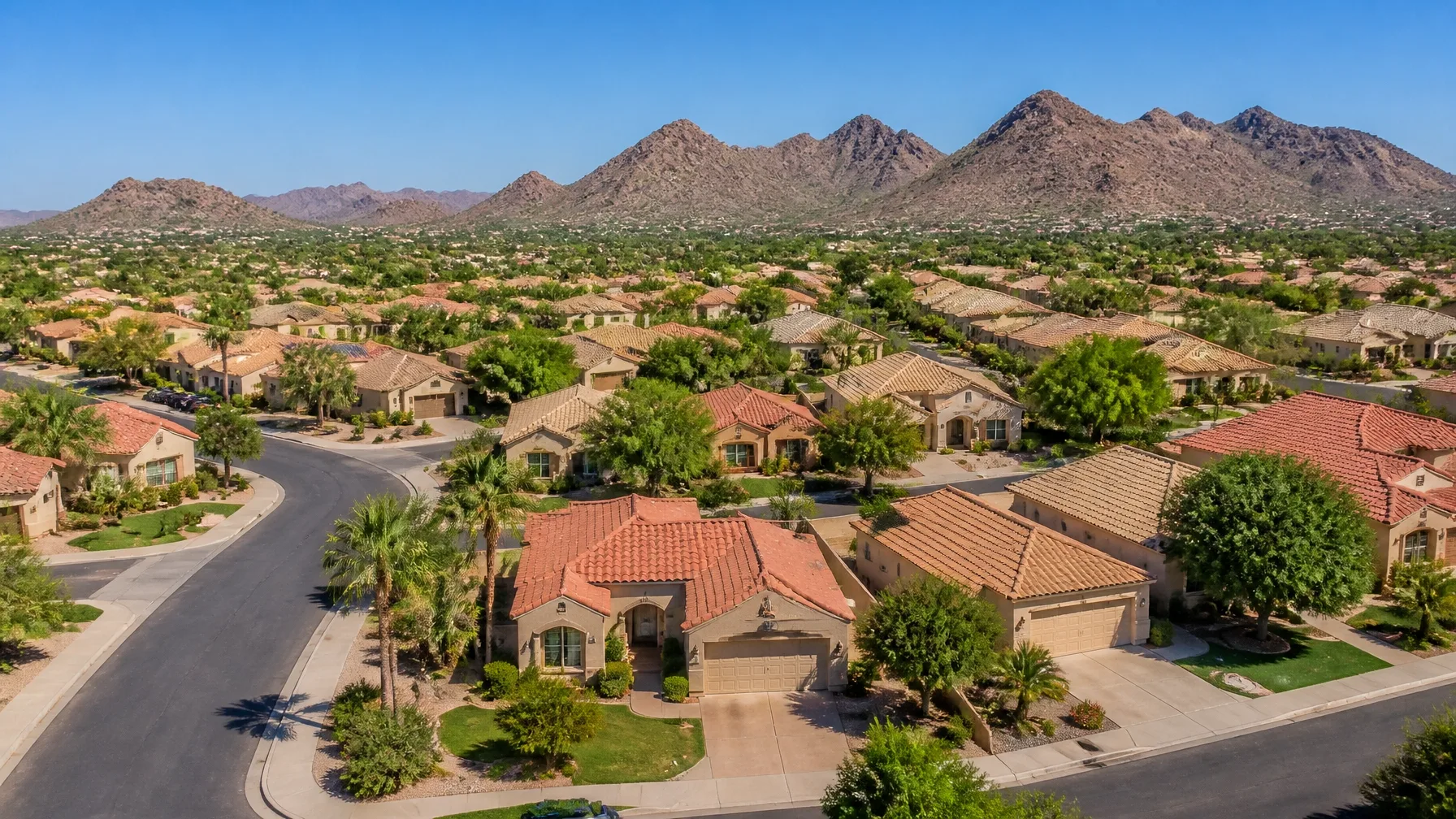 An aerial view of a suburban neighborhood with tan stucco homes, tile roofs, and desert landscaping
