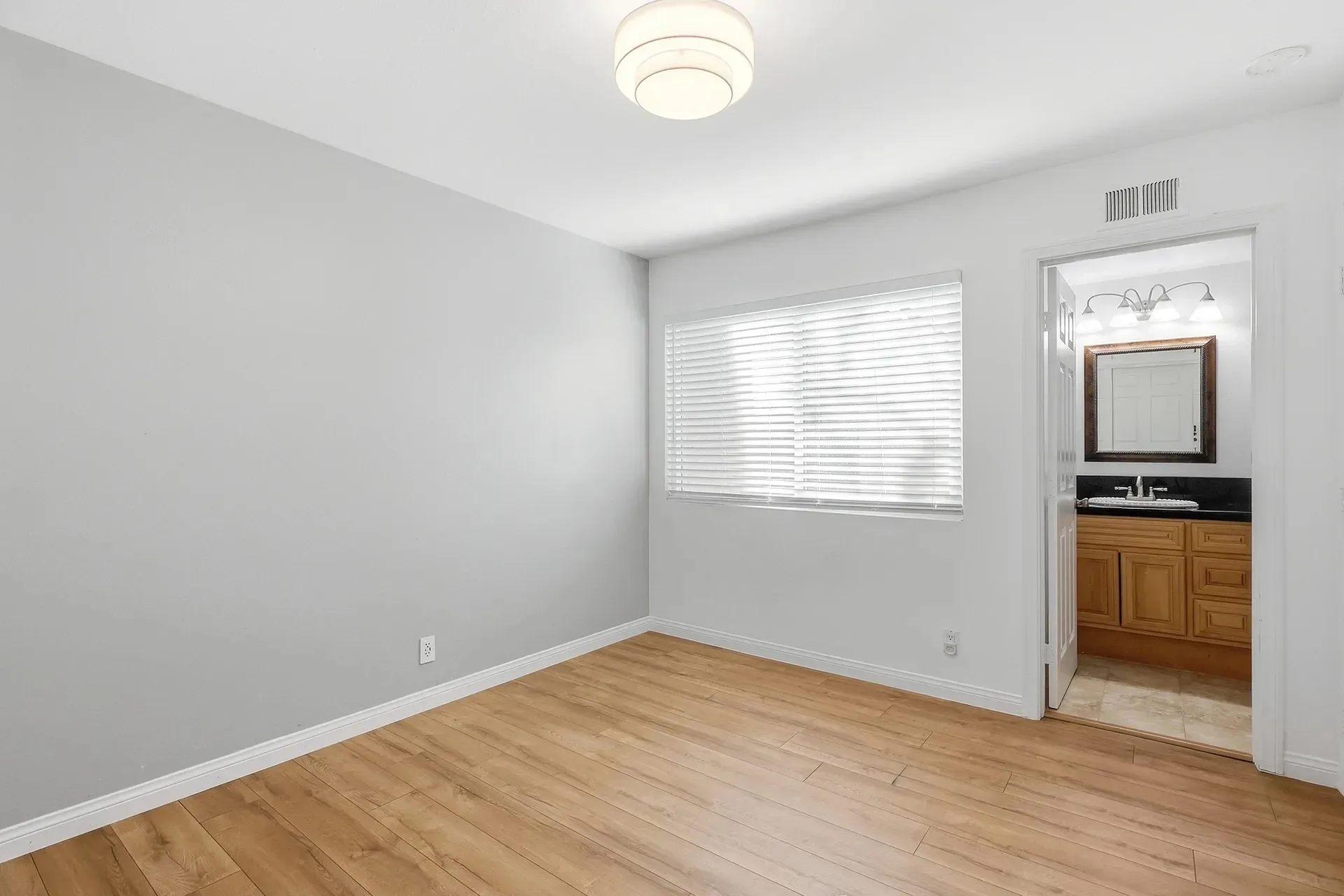 Primary bedroom at 8 Silverwood with light grey walls and wood-look flooring, the attached en-suite bath visible through the doorway