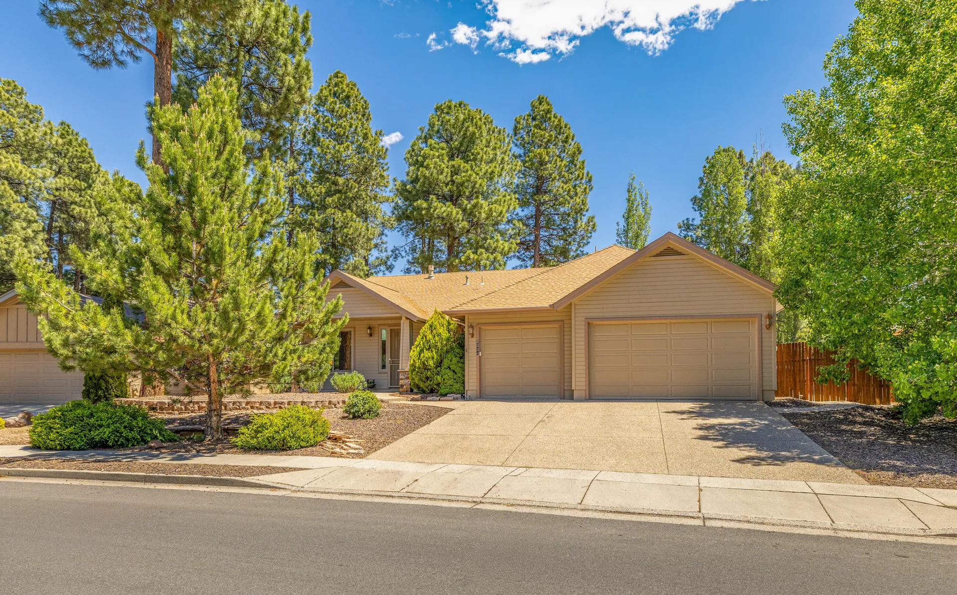 A single-story suburban home with pine trees and desert rock landscaping in a higher-elevation Arizona community