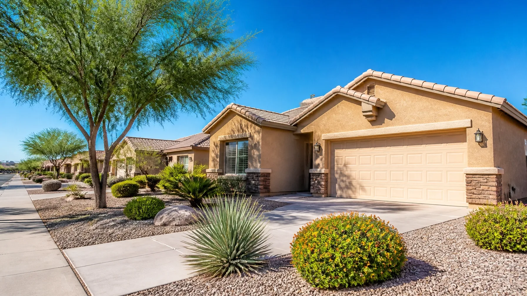 A single-story tan stucco home with a tile roof under a clear blue sky