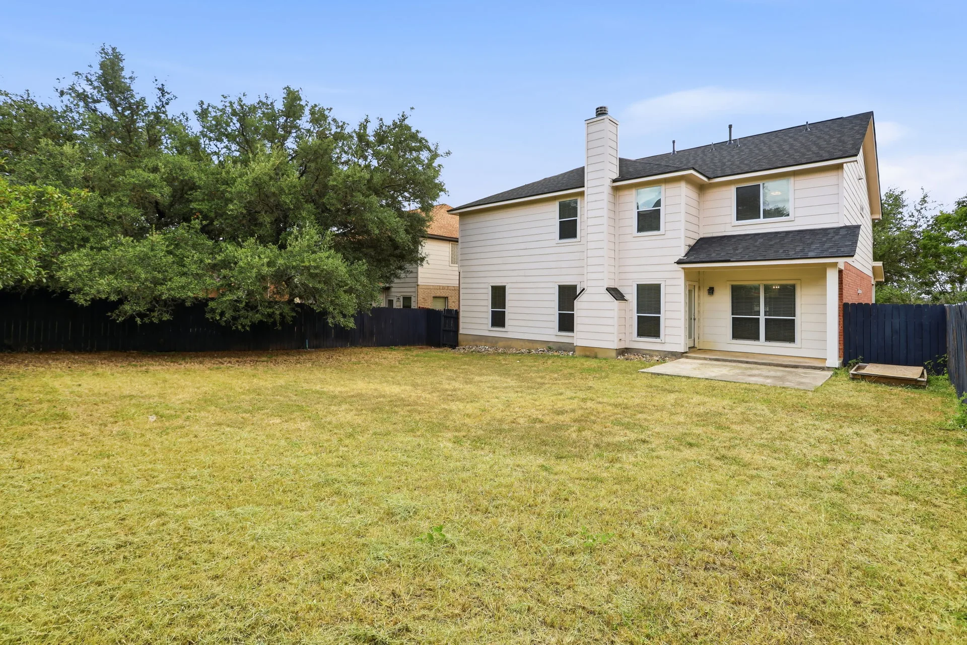 Spacious backyard with a concrete patio and mature oak trees