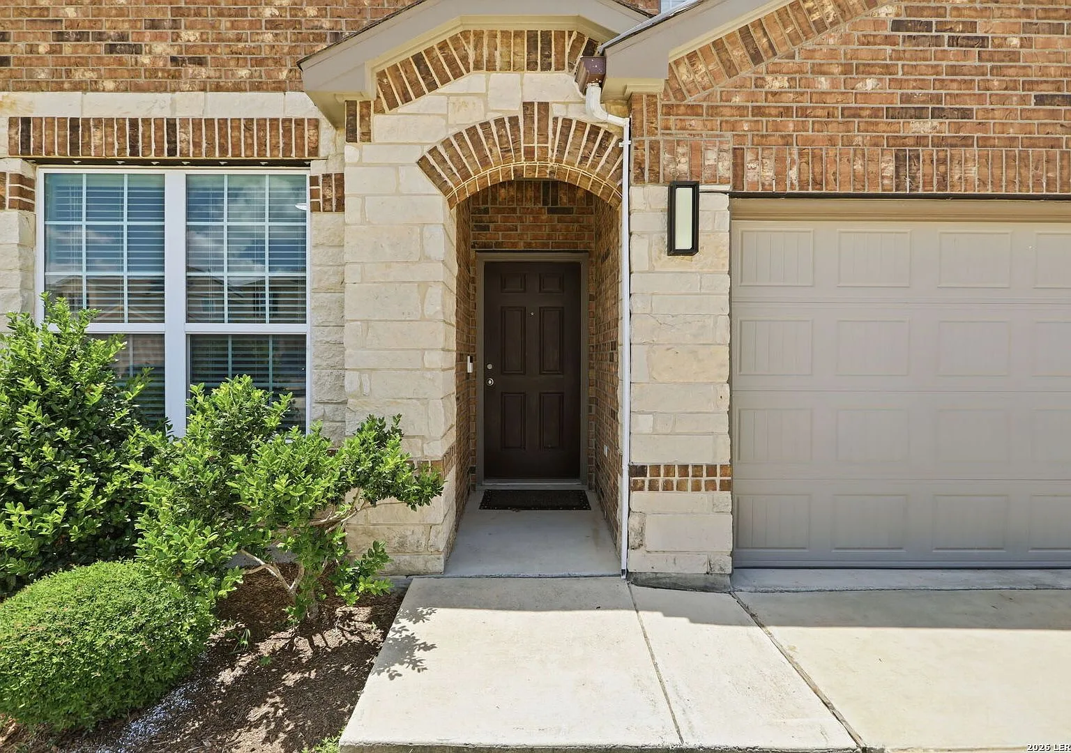 Entry elevation with brick and light stone veneer and a dark wood front door.