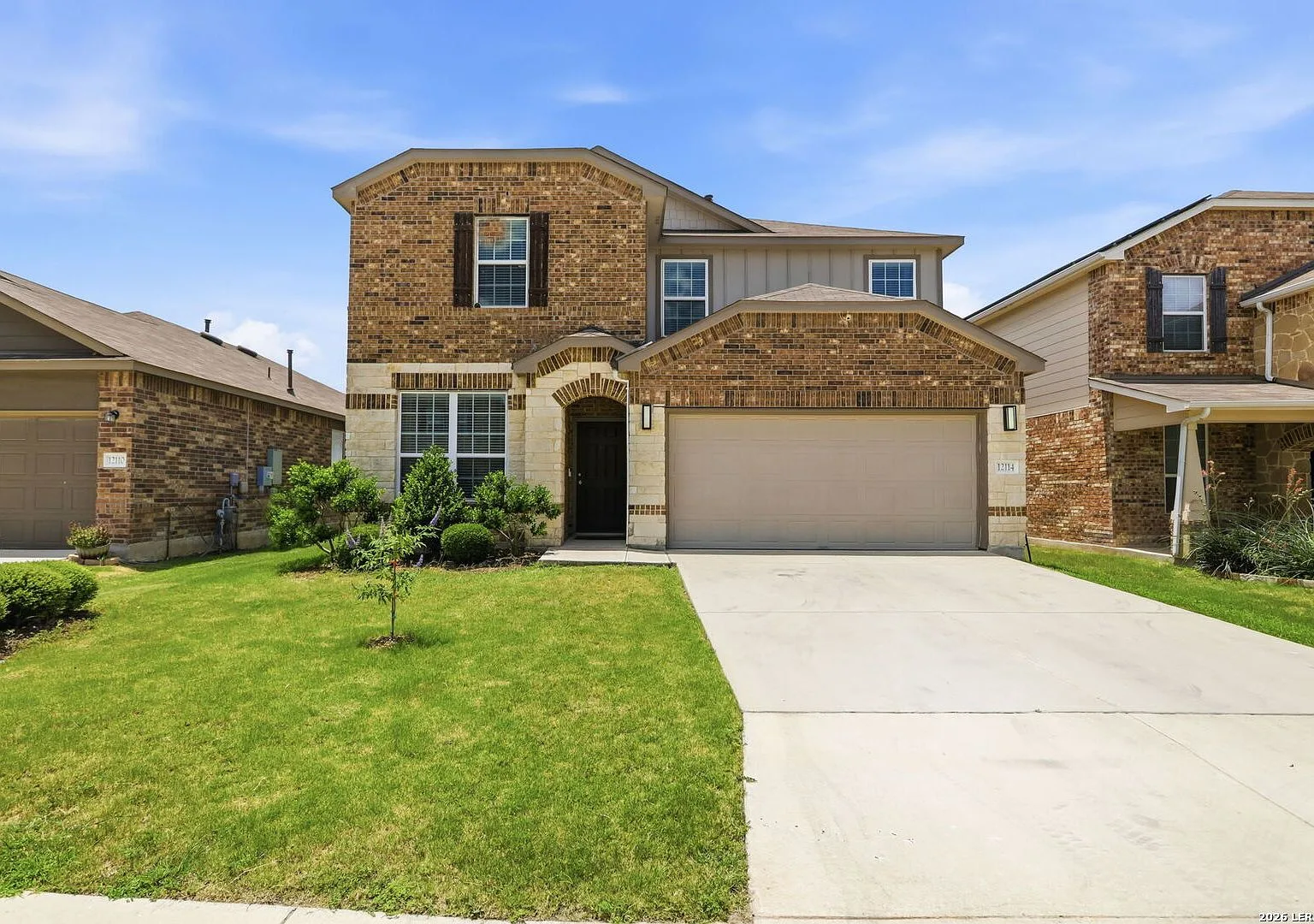 Front exterior of a two-story San Antonio home with tan brick and beige siding in clear daylight.