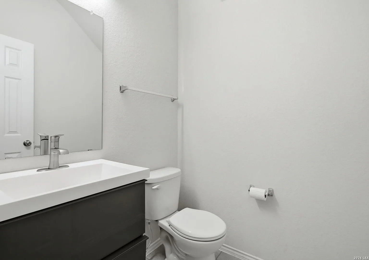 Powder room with a dark grey vanity, white sink, and wall mirror.