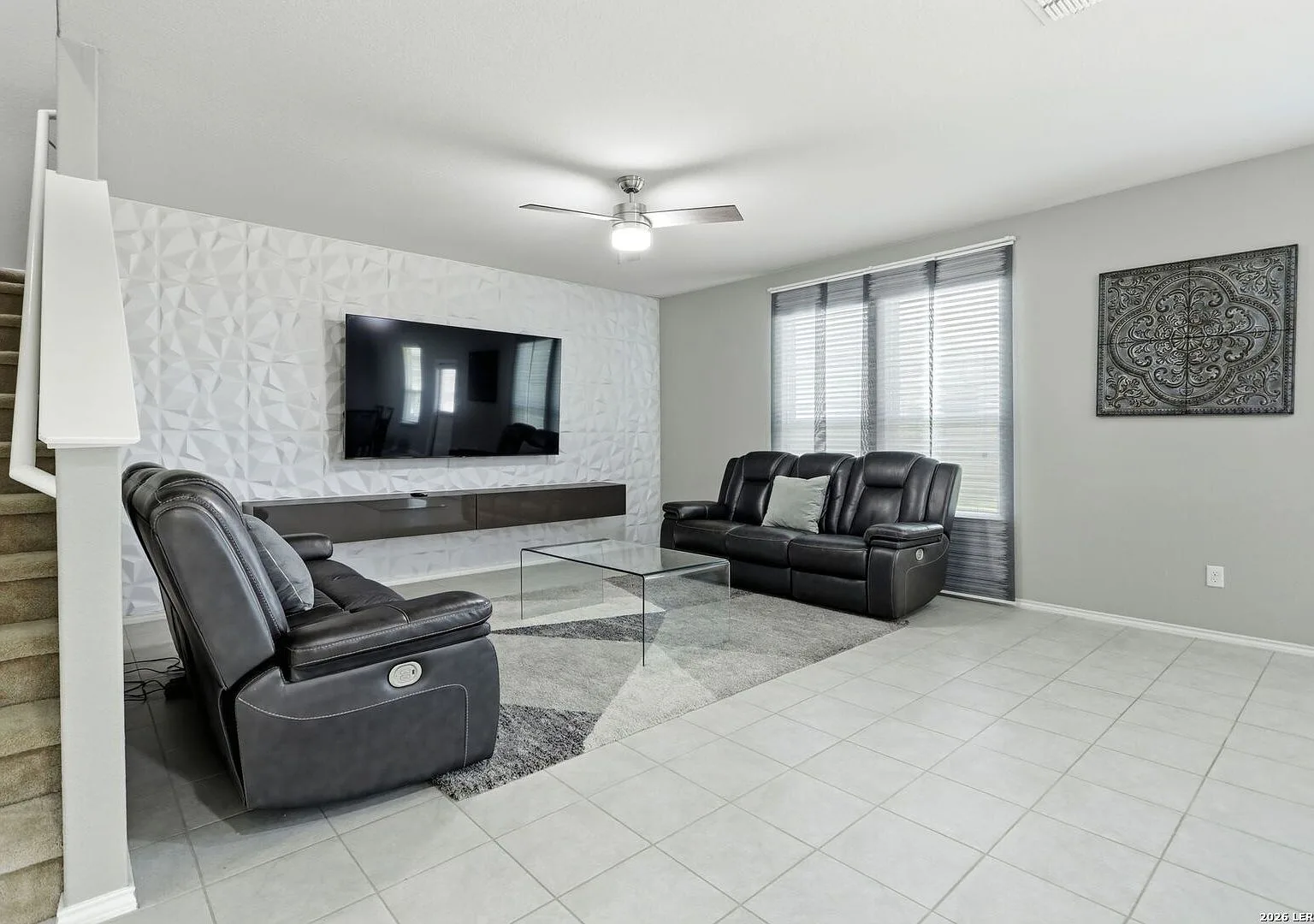 Wide view of the living room with a textured accent wall and neutral grey walls.