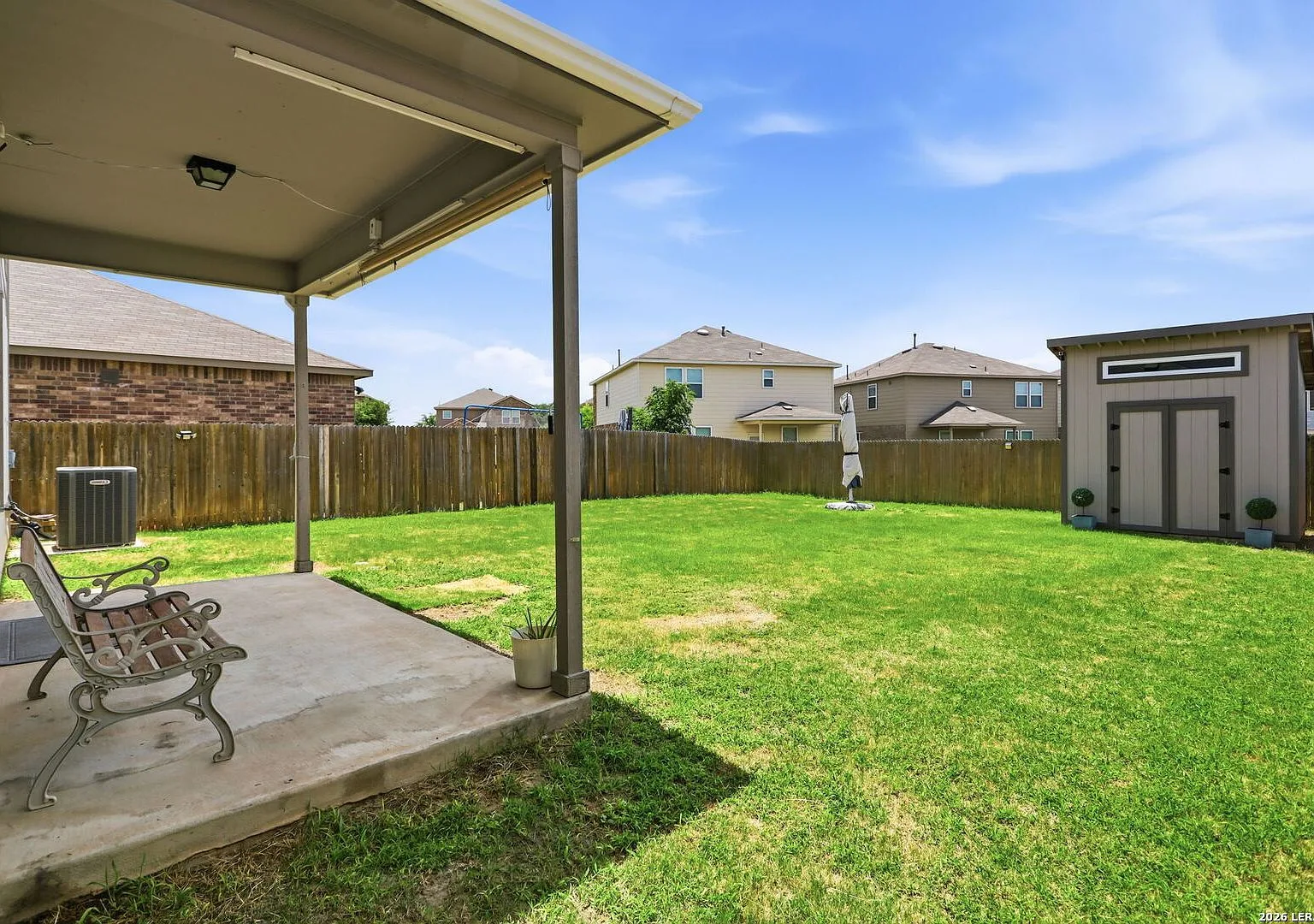 Covered concrete patio off the backyard with privacy wood fencing and lawn.