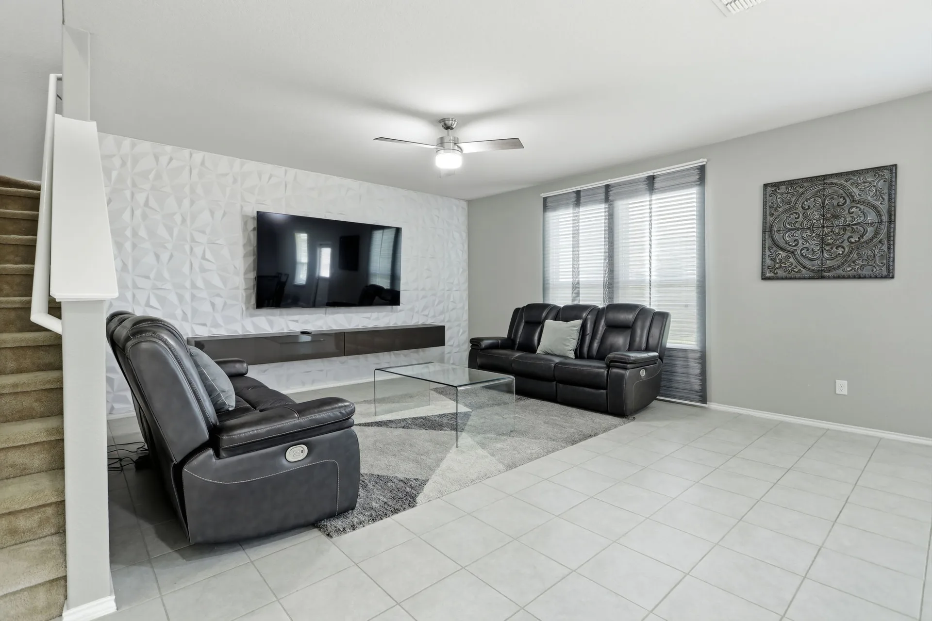 Living room with a white textured accent wall, tile flooring, and an open staircase.