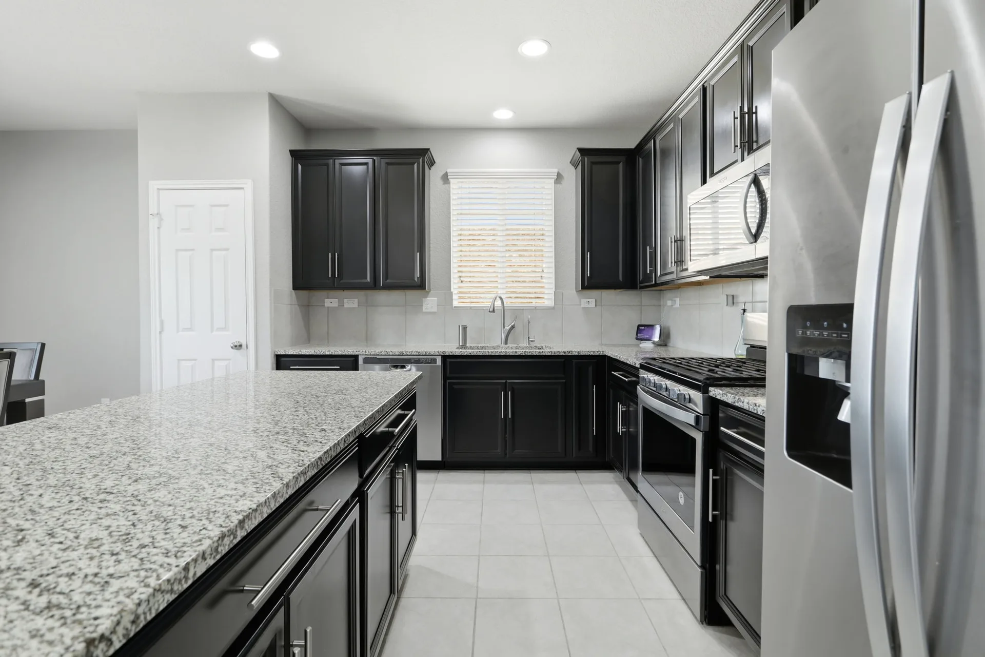 Wide kitchen view with an island, dark cabinets, and a window over the sink.