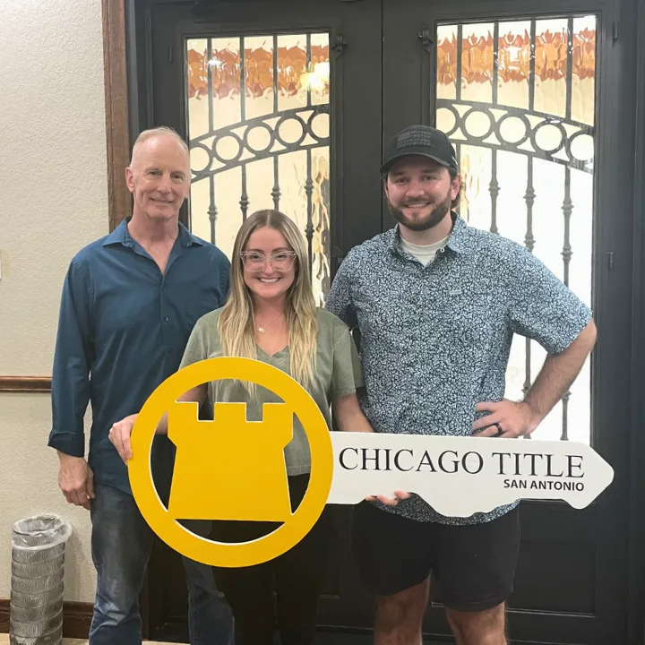 Buyers at the title company closing table with a commemorative key after closing on their home