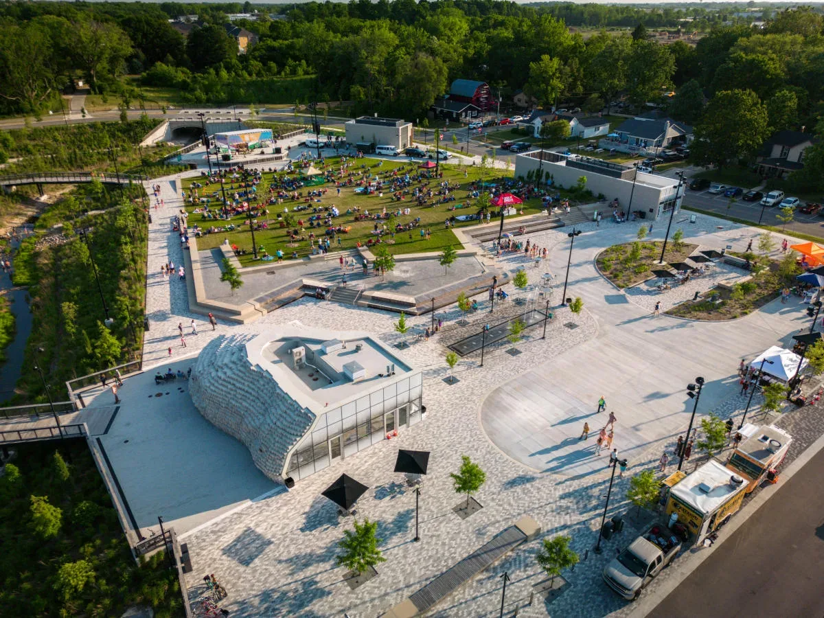 A drone aerial view of a modern community park plaza with a sculpted white pavilion, lawns, and walking paths