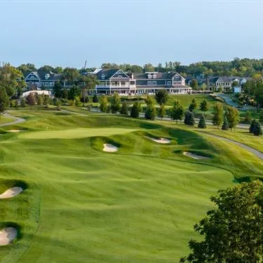 An aerial view of a golf course clubhouse with greens, sand bunkers, and cart paths