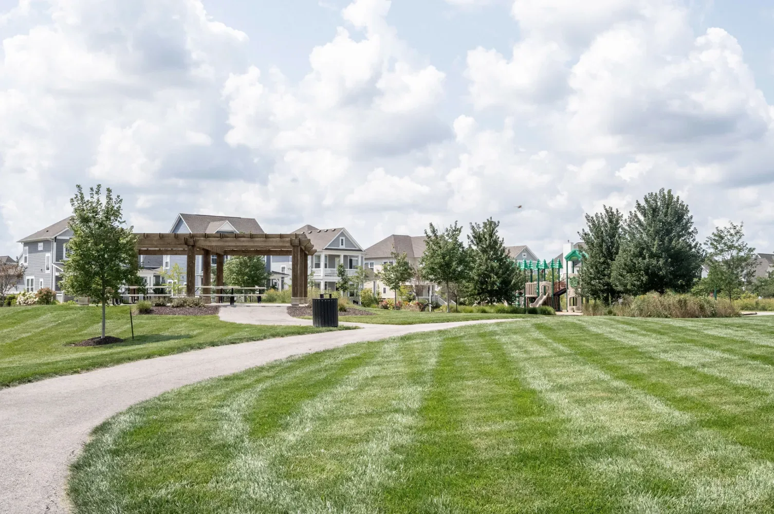 A community park with a wooden pergola, a walking path, and a playground in the distance