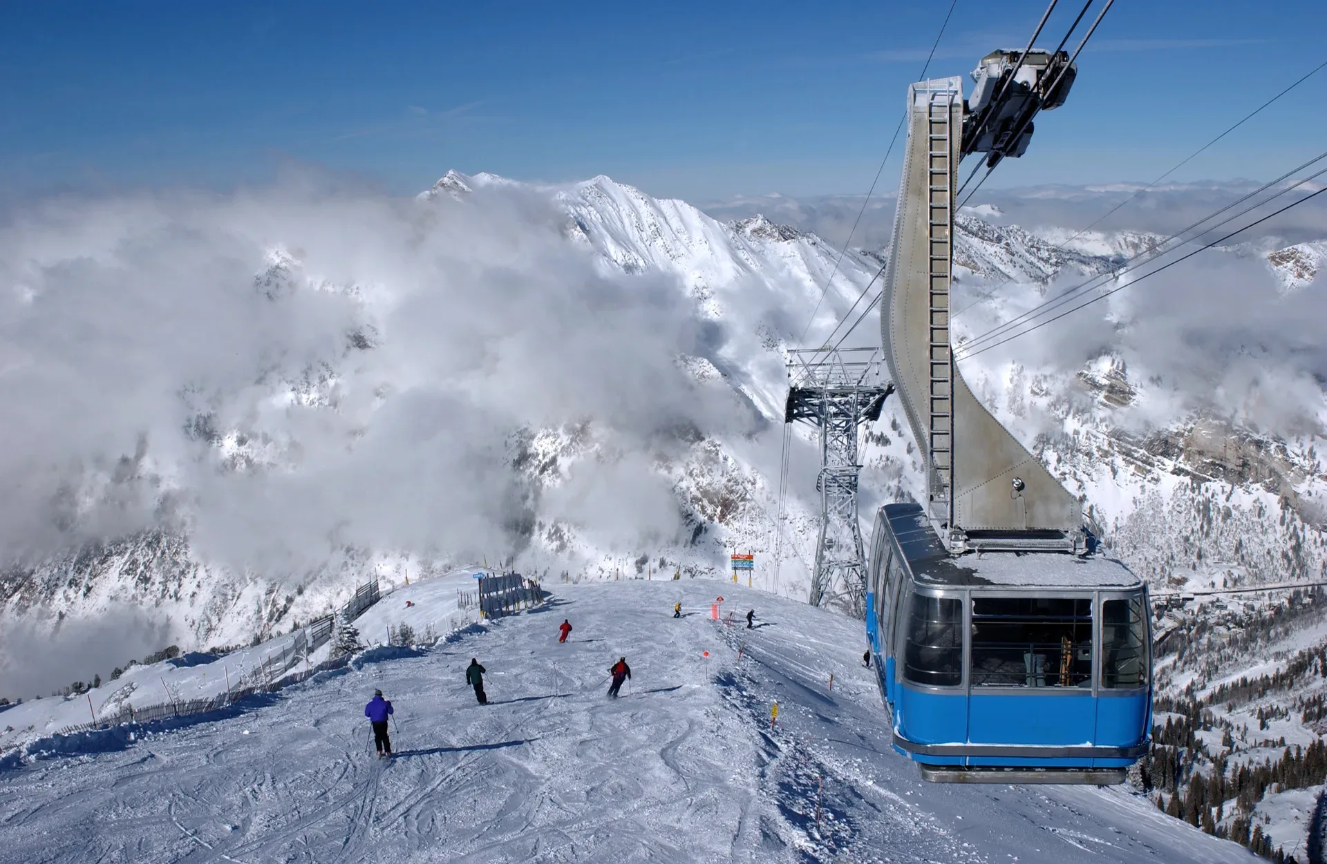 A ski tram climbing above a snow-covered resort run in the Wasatch Mountains under a clear blue sky