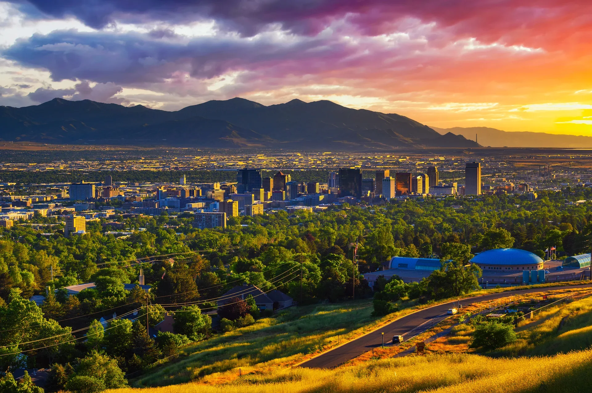 A vivid sunset over a Utah city skyline with purple, orange, and yellow sky above the mountain ranges