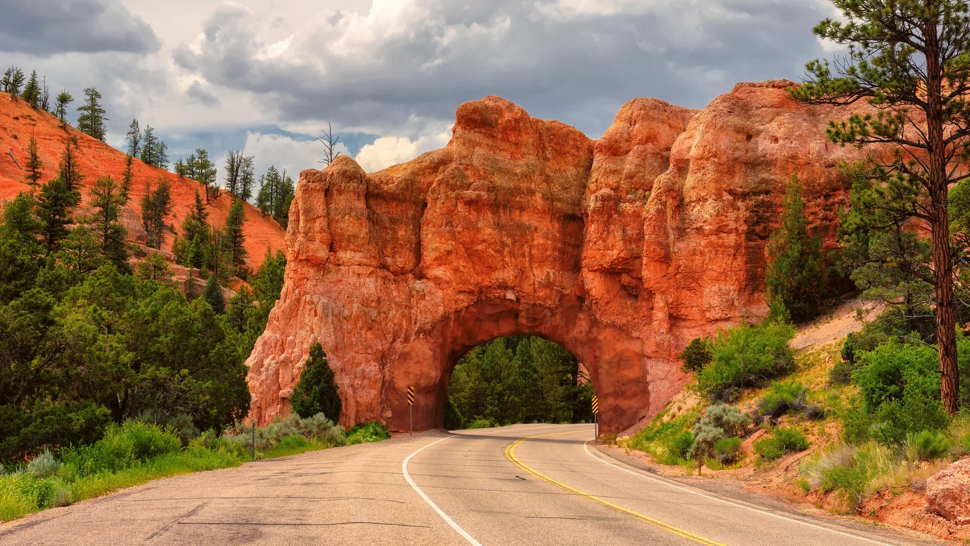 A natural red rock arch forming a tunnel over a winding road in Utah's canyon country
