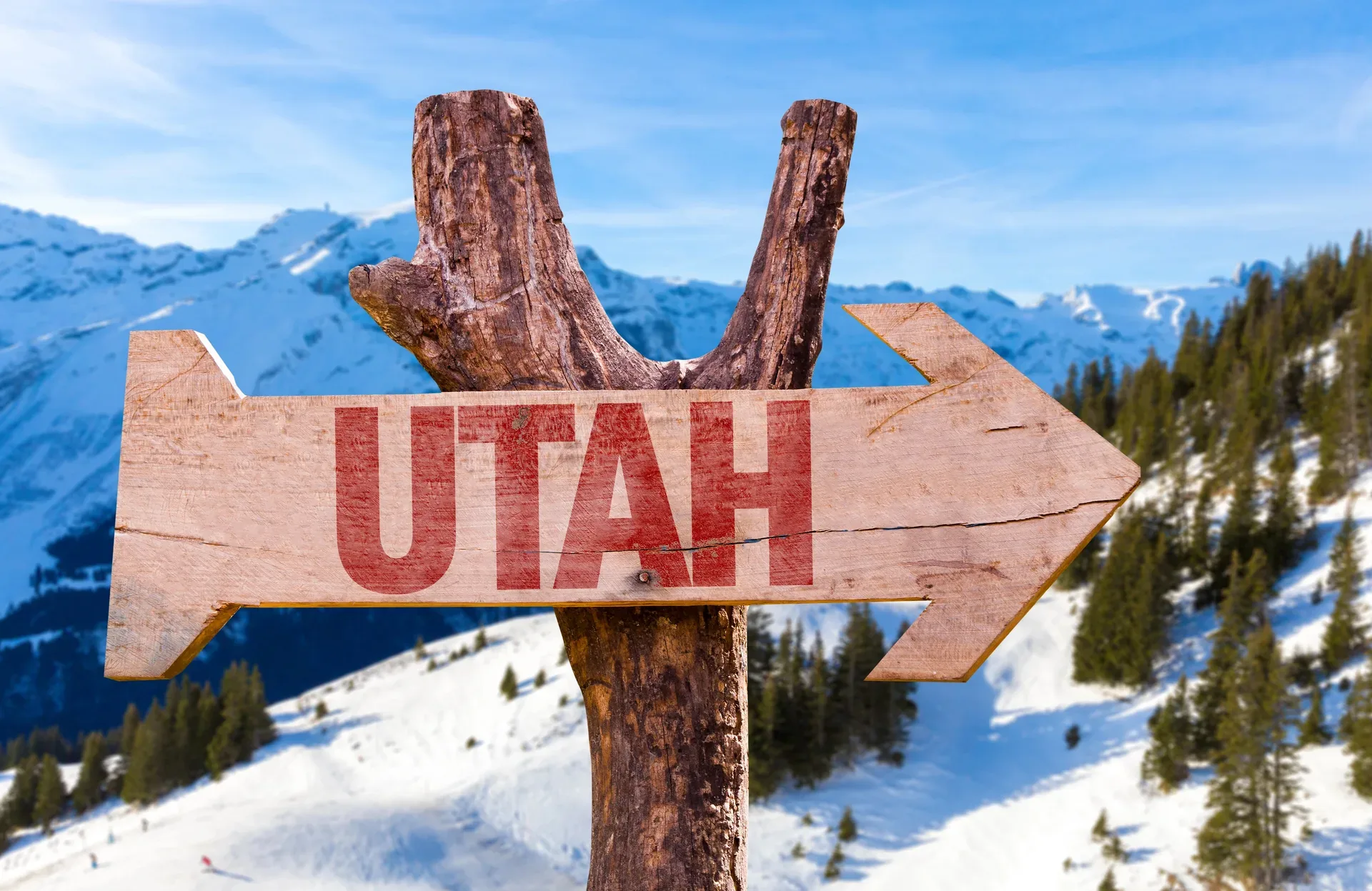 A rustic wooden signpost pointing toward Utah with snowy mountain slopes behind it