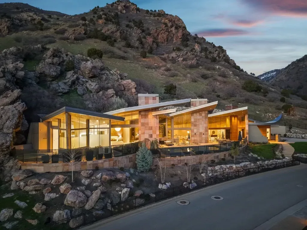 Aerial view of the Canyon Estate Drive mountain-modern estate at dusk, stone and glass glowing against a rocky hillside