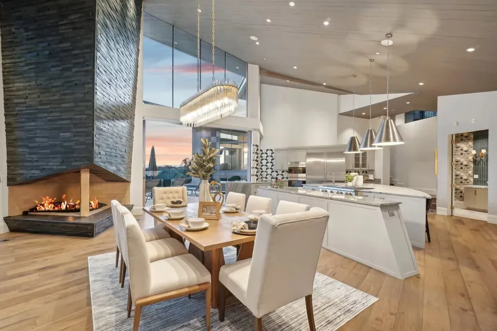 Open kitchen and dining room of the Canyon Estate Drive estate with warm pendant lights and a stone fireplace