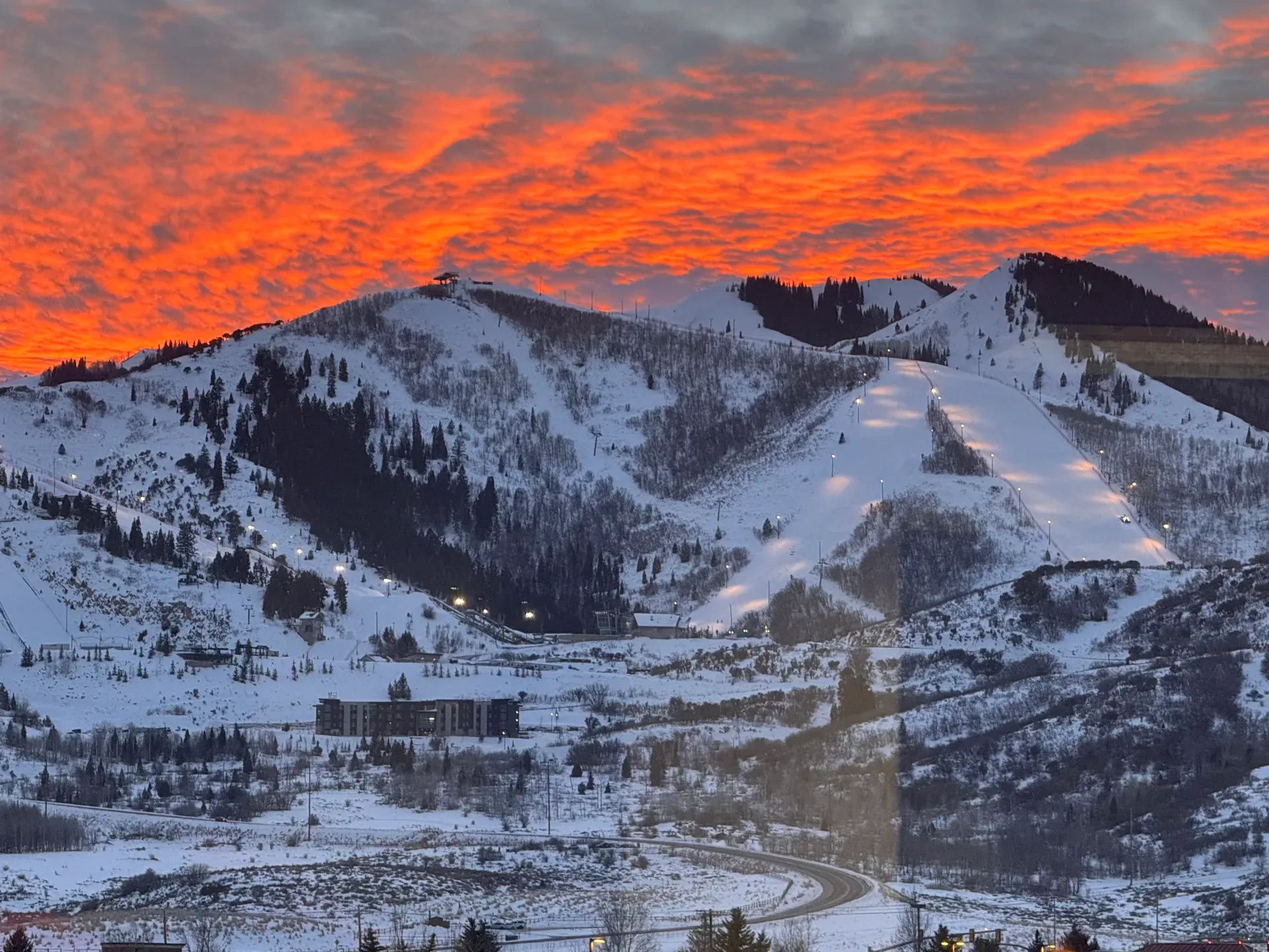 Snow-covered ski slopes and ridgelines under a dramatic fiery sunset sky in the Wasatch