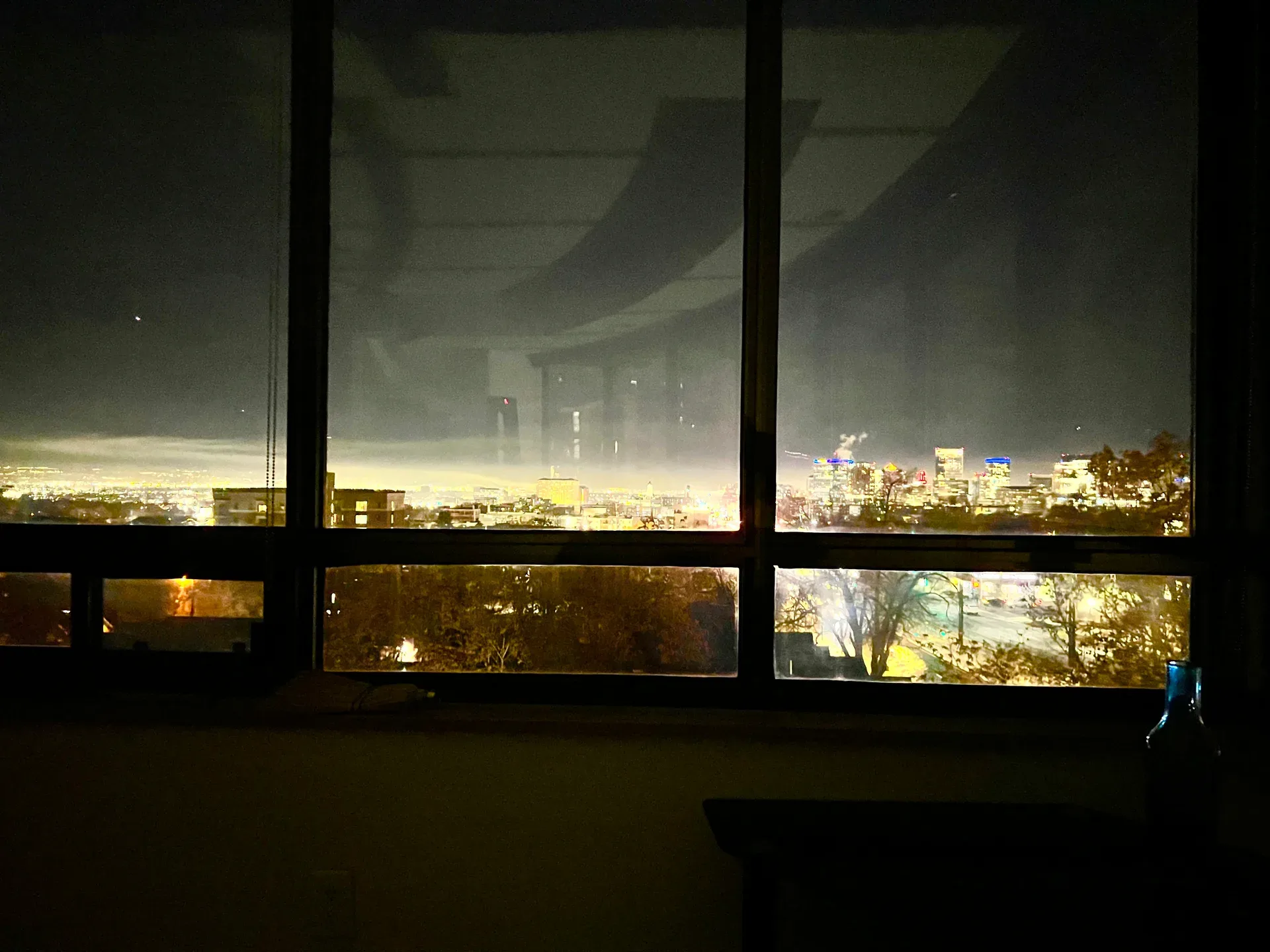 City lights glowing through a large picture window at night over an illuminated cityscape