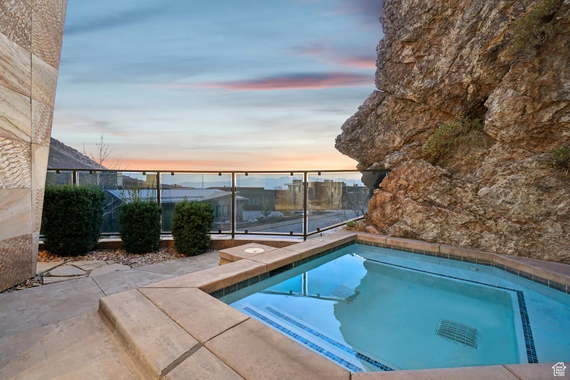 A built-in hot tub on a stone patio set against a large natural rock formation at sunset