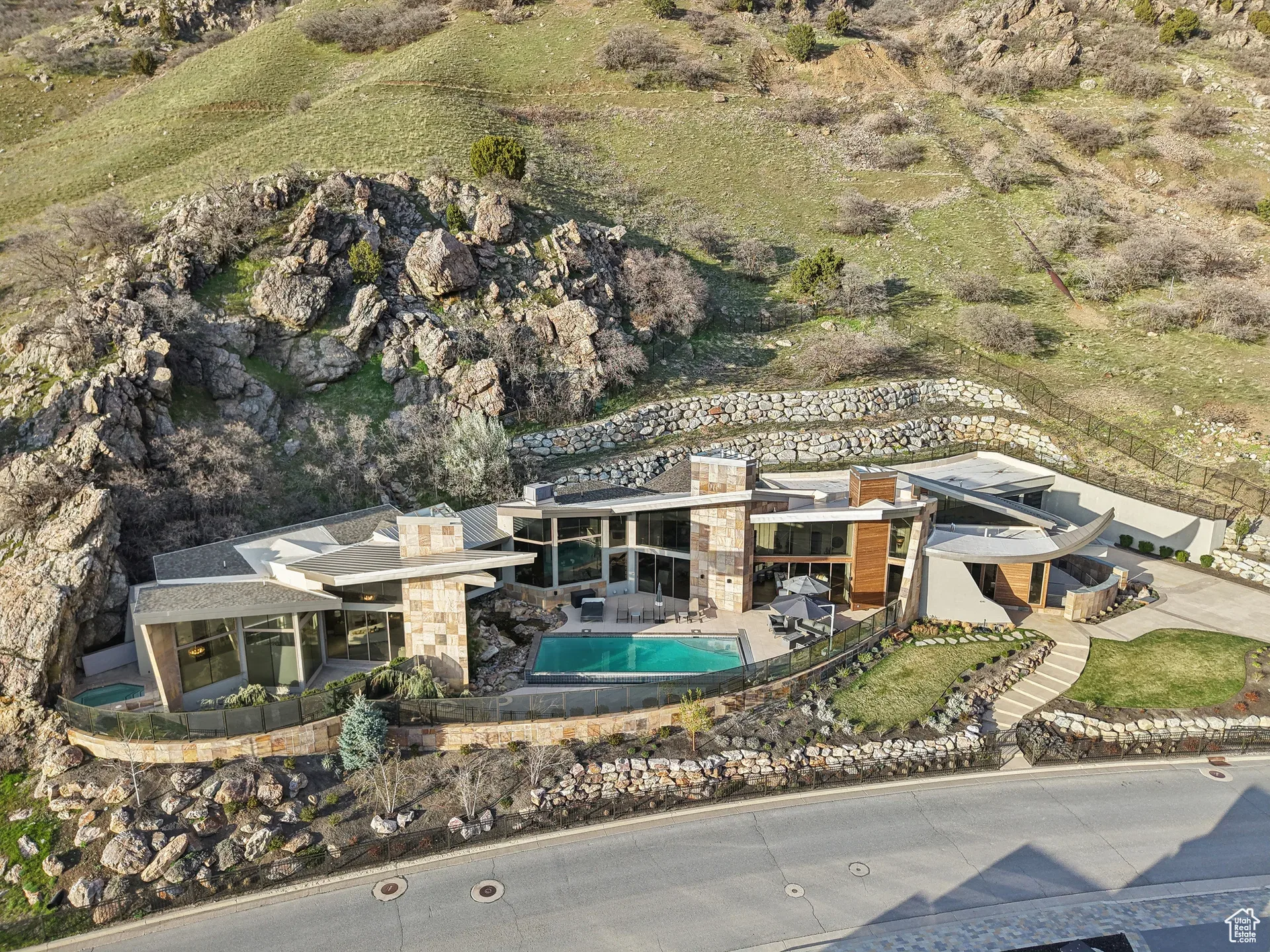 Aerial view of a mountain estate with stone and stucco architecture set into a hillside in daylight