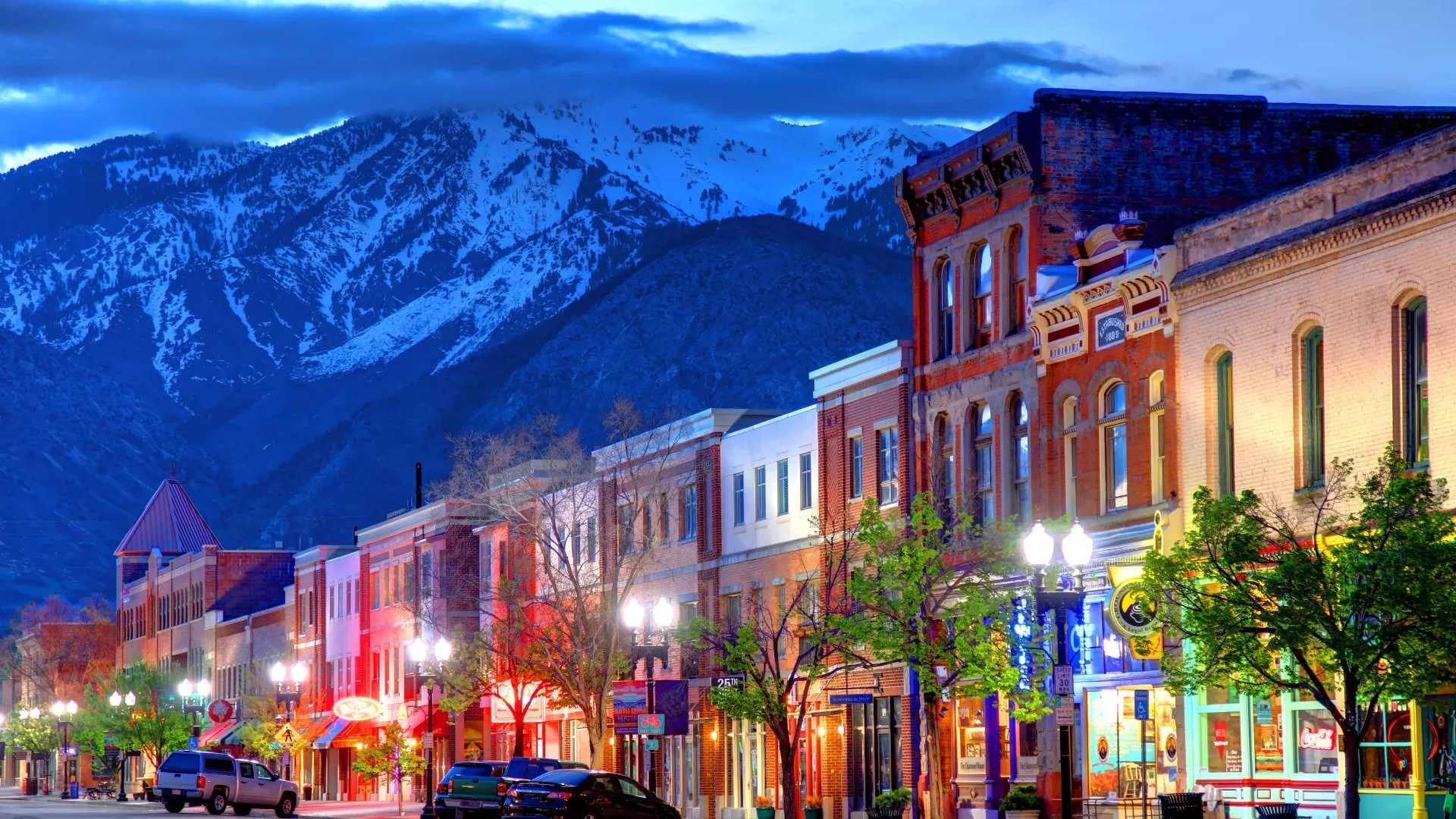 Park City's historic Main Street at twilight, brick storefronts and lit street lamps beneath snow-capped peaks