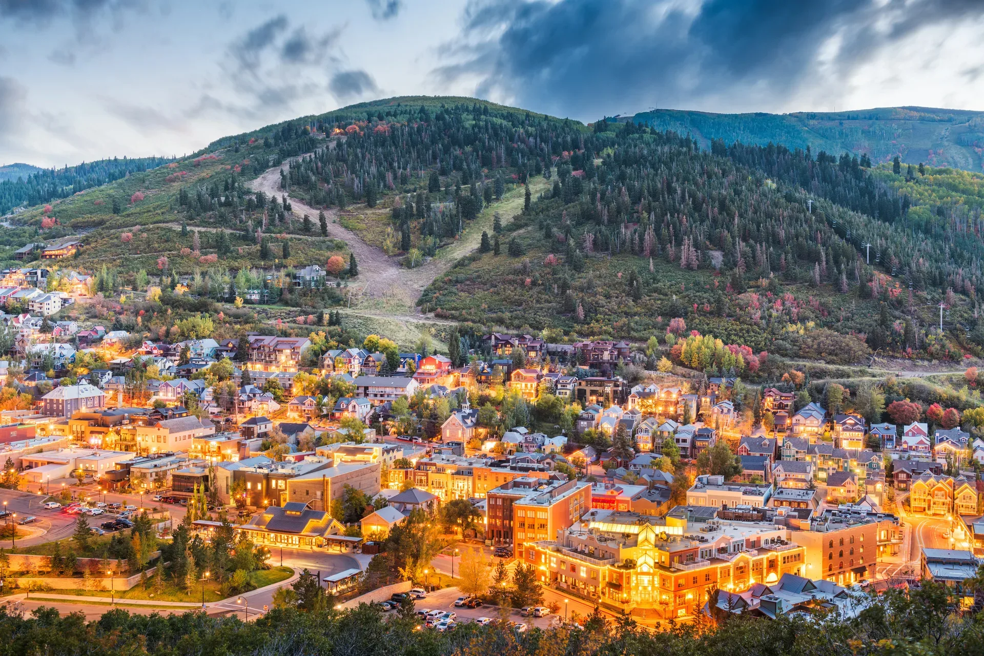 Aerial view of Park City, Utah at dusk with mountain town rooftops glowing beneath the surrounding peaks