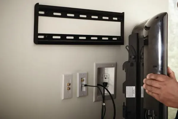TV wall mounting job in San Antonio: a handyman fixing a metal TV mount bracket to the wall with a flat-screen television held in place