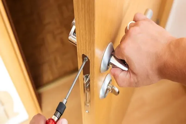 Door handle repair in San Antonio: a handyman installing brushed-metal door hardware on a wood door with a screwdriver
