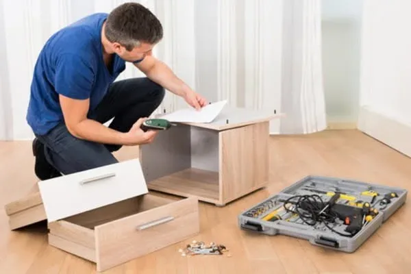 Furniture assembly service in San Antonio: assembling a light-wood cabinet with a toolkit and power drill on a hardwood floor