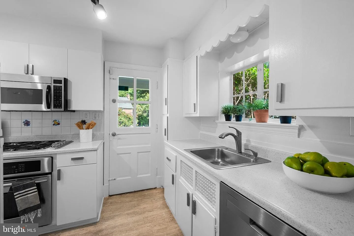 Updated kitchen with white cabinets, light countertops, and stainless steel appliances