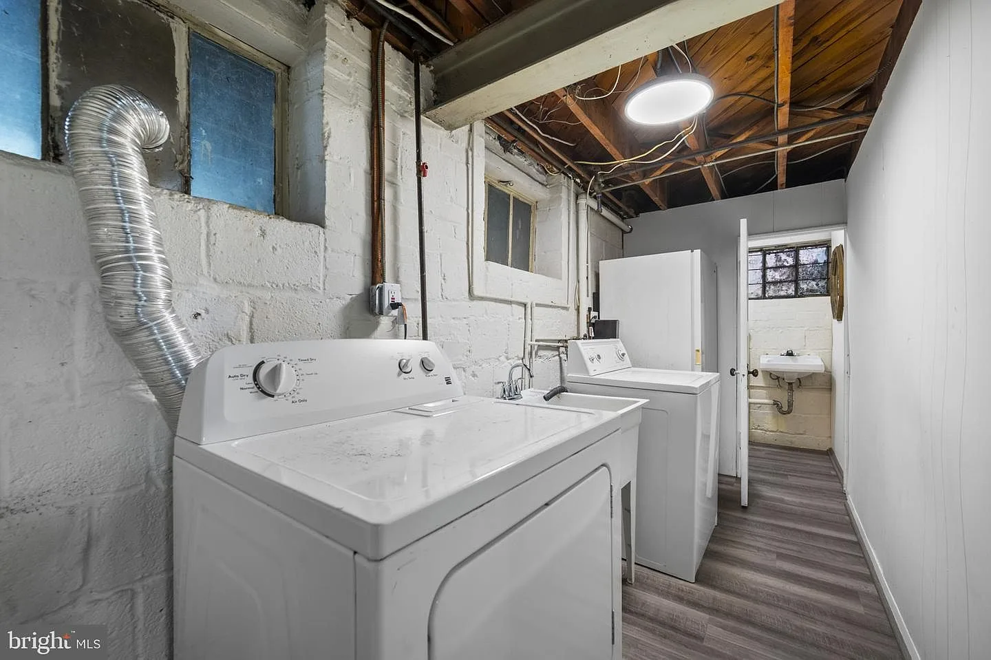 Basement utility area with painted brick, vinyl plank flooring, and laundry