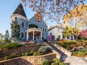 A blue Victorian house with a turret and wrap-around porch on an Avenues street